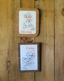 Two framed embroidery pieces with vintage cowboy illustrations hanging on a rustic wooden wall. The top print has a light wood frame and says 'Saturday', while the bottom print has a dark wood frame and says 'Friday'.