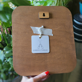 A wooden embroidery hoop frame with a keyhole cutout at the top, held by a hand with red nail polish. A white tag reading 'EMBER 8 THREAD' is attached with tape.