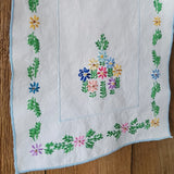 A square white embroidered vintage wall hanging with a light blue border and colorful floral motifs