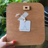 square wooden board with rounded corners, featuring a small wooden loop at the top and a hanging paper tag that reads “EMBER & THREAD.” 