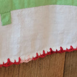 A close-up of a textile product showing a white woven fabric section with a red zigzag stitched edge