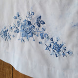 Light blue dyed fabric with a delicate blue floral embroidery pattern, laid over a wooden surface.